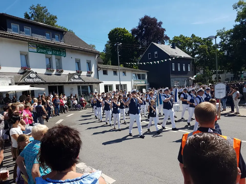 Das Tambourkorps beim Festzug, rechts das getragene Schild mit dem Vereinsnamen, links die Zuschauerreihen